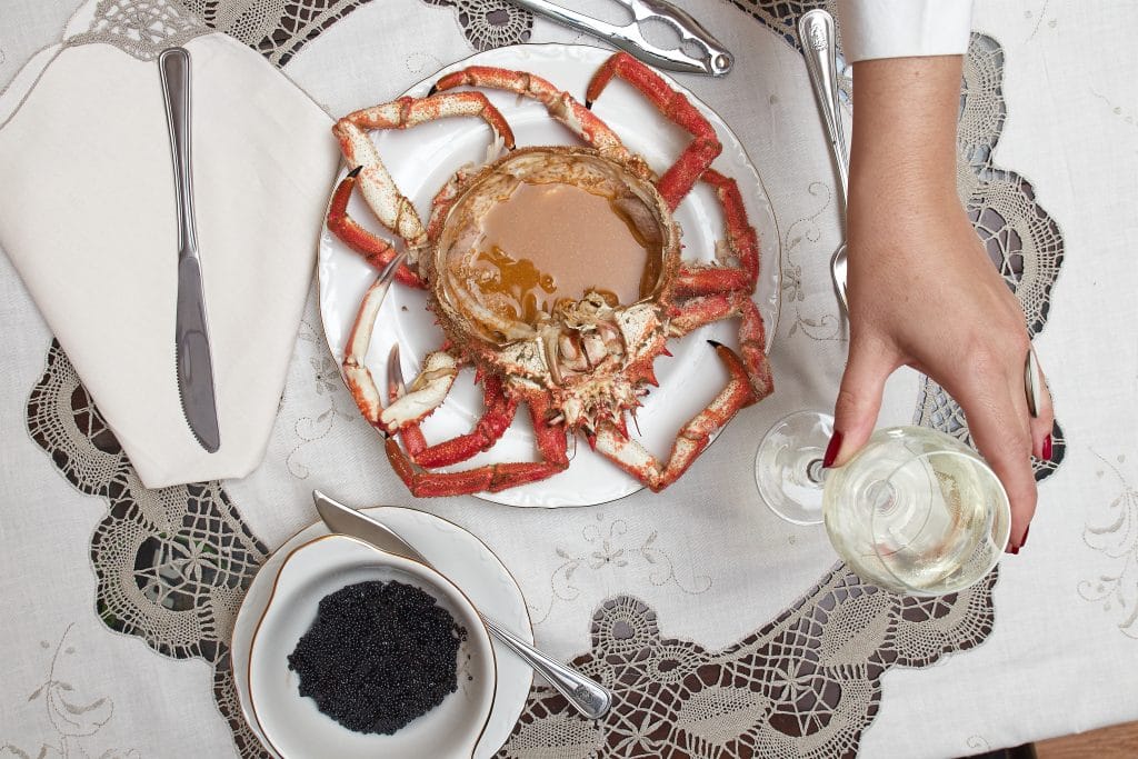 Woman hands is taking white wine and there is a big red cooked spider crab in a luxury dinner with white wine and black caviar